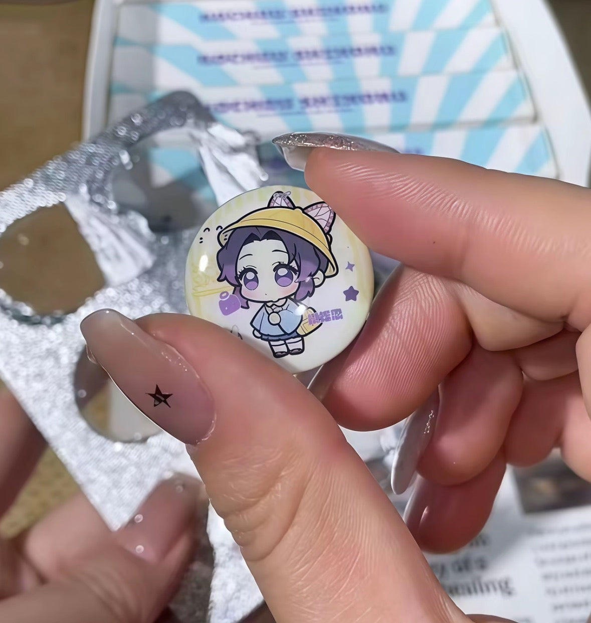 Hand holding a round badge with an illustration of a character against a blue and white striped background.