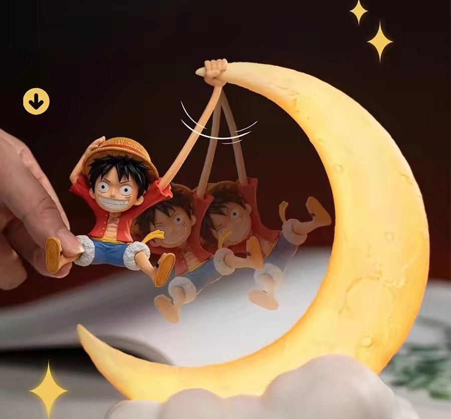 Figurine of a character on a crescent moon with another character underneath, set against a dark background.