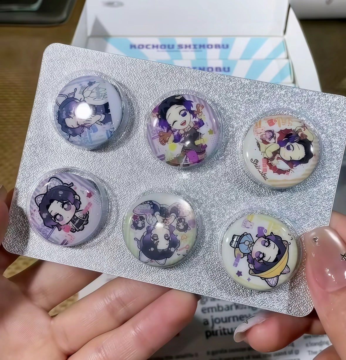 Set of six cartoon character buttons in a packaging holder held by a person.